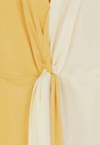 Panneaux de tissu doux jaunes et blancs torsadés ensemble en un nœud central.