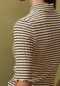 Pasiasty dzianinowy top z krótkimi rękawami, z beżową bazą i ciemnobrązowymi poziomymi paskami. Ząbkowany dół i szczegół kołnierzyka.