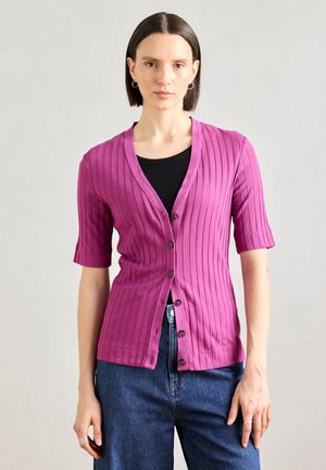Fuksia ribbet cardigan med korte ærmer, V-hals, frontknapper, teksturert stoff, kombinert med en svart topp og blå jeans.