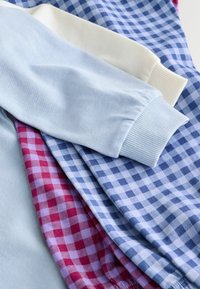 Warstwy odzieży bawełnianej w jasnoniebieskim, kremowym kolorze oraz w dwóch kratkach (czerwono-różowej i niebieskiej) z prążkowanymi mankietami i gładką teksturą.