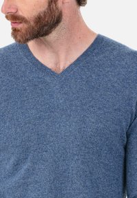 Pull col en V d'un bleu moyen, confectionné dans un tissu doux et texturé, avec une coupe classique et des détails côtelés subtils au niveau de l'encolure.