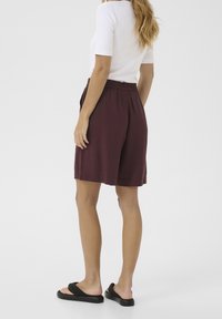 Shorts bordeaux con elasticità in vita, realizzati in tessuto morbido, caratterizzati da una vestibilità comoda e orlo dritto. Indossati con sandali neri a ciabatta.