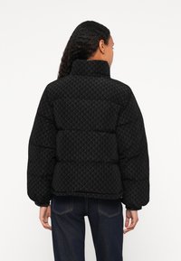 Czarna puchowa kurtka z wysokim kołnierzem i geometrycznym wzorem. Posiada pikowane sekcje, szerokie rękawy i skrócony krój.