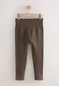 Braune gerippte Leggings mit einem strukturierten Bund, an einem Holzkleiderbügel vor einem hellen Hintergrund hängend. Glatte Textur, ganzes Bein lang.