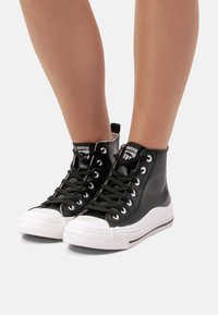 Sneaker alte nere in pelle liscia, con suole in gomma bianca, lacci neri e un'etichetta del brand sulla linguetta.