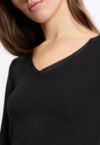 Czarna bluzka z długim rękawem z dekoltem w serek, ozdobiona delikatną koronką. Miękka, gładka tkanina o dopasowanym kroju.