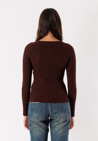 Maglione marrone a coste con maniche lunghe, dal design aderente e scollatura rotonda, abbinato a jeans blu a vita alta con leggeri segni di usura.