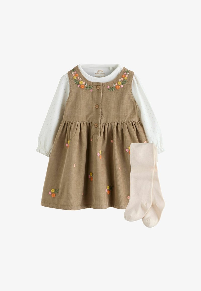 Abito per bambina in corduroy beige con ricami floreali su una maglietta bianca a maniche lunghe con piccoli punti, abbinato a collant beige chiaro.