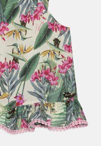 Top senza maniche floreale con stampa tropicale che presenta fiori rosa, foglie verdi e colibrì. Orlo arricciato con bordino rosa e dettaglio del logo.