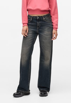 Wide-leg jeans in dark wash denim with a faded finish. Features classic five-pocket design and metal hardware. Paired with a pink hoodie.