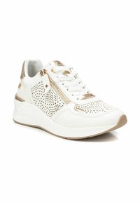 Zapatilla blanca con acentos metálicos dorados, textura de cuero y perforaciones, diseño de cordones, detalle de cremallera lateral y suela blanca gruesa.