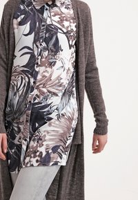 Gray open cardigan over a floral button-up shirt in shades of blue and beige. The shirt features a collar and a tropical leaf pattern.