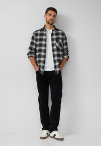 Koszula flanela w czarno-białą kratę, w połączeniu z białą koszulką, ciemnymi spodniami i białymi trampkami z szarymi akcentami.