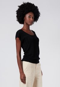 Suéter negro de punto de manga corta con patrón texturizado, cuello redondo y bajo acanalado. El modelo lo combinó con pantalones de color claro.