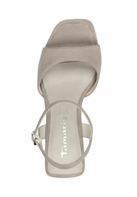 Beige mockasin-högklackad sandal med ett brett övre rem, en vristrem och en fyrkantig tådesign. Har en platt innersula och diskret logotypdetalj på insidan.