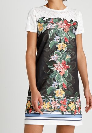 Kurzes Kleid mit weißen Spitzenärmeln, schwarzem Vorderteil mit farbenfrohem Blumenmuster und weißem Saum mit blauen Streifen.