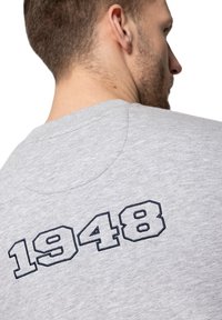 Szara koszulka z okrągłym dekoltem, krótkimi rękawami i haftowanym na granatowo napisem "1948" na plecach. Miękka bawełniana faktura.