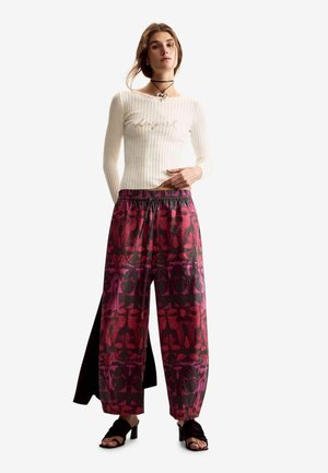 Top crema a maniche lunghe a coste abbinato a pantaloni a gamba larga con motivo astratto rosa e nero. Il look è completato da sandali neri con tacco.