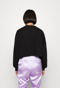 Felpa nera tagliata con maniche lunghe, scollo rotondo e una consistenza morbida, abbinata a pantaloni in satin lavanda lucido.