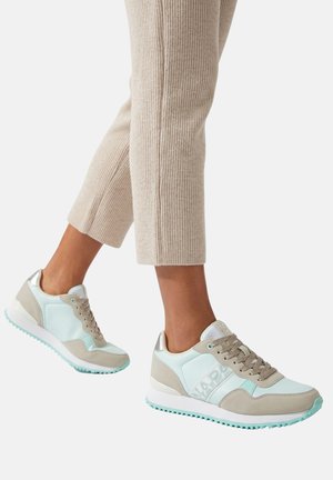 Gambe con pantaloni a coste beige e sneaker azzurro chiaro e beige con lacci e suola bianca.