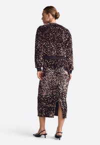 Suknelė su švytinčiais akmenėliais tamsiai rudos ir rožinės aukso atspalvių, turinti pritaikytą liemenį ir nugaros skeltuką. Ilgos rankovės su gumbuotais raiščiais.