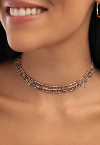 Collar choker de múltiples hebras hecho de pequeñas cuentas coloridas en púrpura, naranja y dorado, con una textura suave y forma circular.