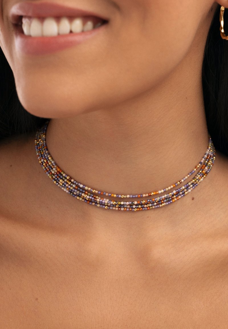 Collar choker de múltiples hebras hecho de pequeñas cuentas coloridas en púrpura, naranja y dorado, con una textura suave y forma circular.