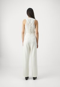 White sleeveless top with a buttoned back, paired with high-waisted white wide-leg trousers featuring two back pockets and subtle seams.