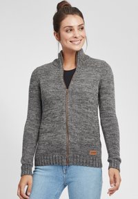 Gray knitted sweater with a high collar, full zipper, and ribbed cuffs, featuring a leather tag on the bottom left side.