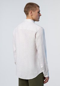 Camicia a maniche lunghe bianca a righe con una texture morbida, polsini con bottoni, orlo curvo e colletto standard, abbinata a pantaloni verde oliva.