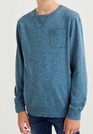 Sweat-shirt bleu à manches longues avec de subtiles mouchetures noires, poche poitrine, poignets et ourlet côtelés, porté par une personne debout.