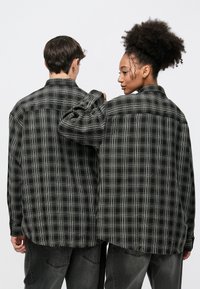 Fekete és szürke kockás, gombos ing laza szabással, gallérral, hosszú ujjakkal és egyenes aljú hátsó résszel.