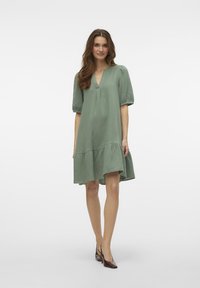 Zelena, neobavezna haljina s V-izrezom, napuhanih rukava i slojevitim rubom. Izrađena od teksturiranog materijala za ležeran izgled.