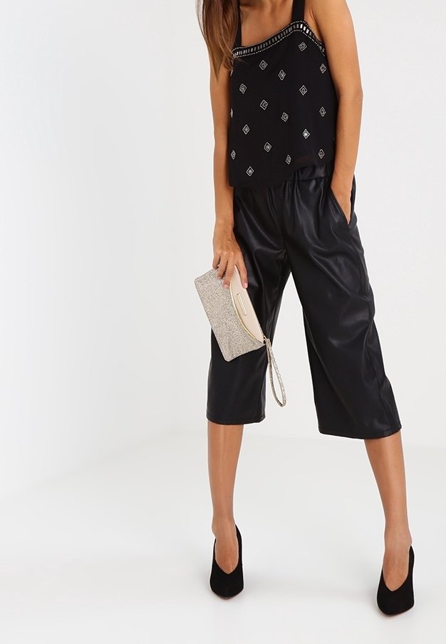 Svart ärmlös topp med geometriskt silvermönster, kombinerad med svarta korta byxor i konstläder. Tillbehöret är en beige clutchväska.