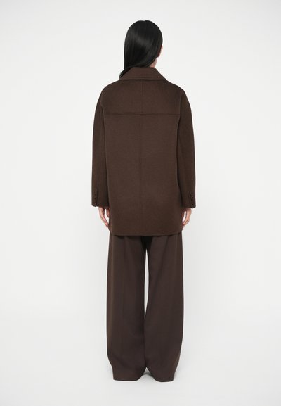 Manteau oversize en mélange de laine marron avec un col cranté, une silhouette droite et trois boutons sur chaque manchette. Associé à un pantalon marron à jambes larges.