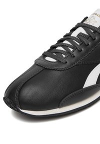 Mustast nahast toss valgete detailidega, millel on ümmargune nina, tekstuuriga pind, lamedad mustad paelad ja mustriga kummist tallad.