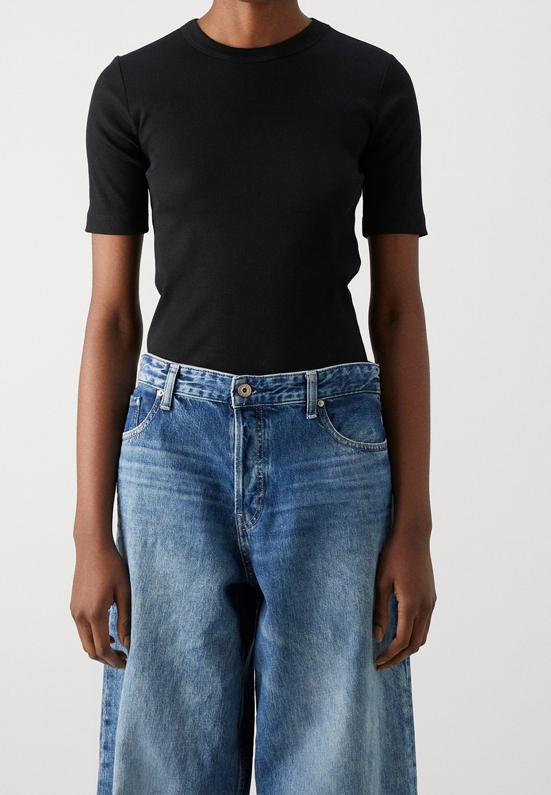 Svart ribbad t-shirt med kort ärm, i kombination med ljusblå vida jeans med knappstängning och framfickor.