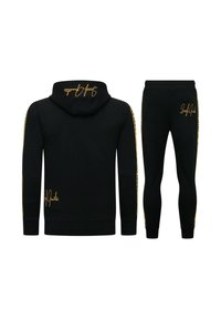 Zwarte hoodie en joggingset gemaakt van zachte stof, met gouden accenten en kenmerkende branding op de capuchon en het broekbeen.