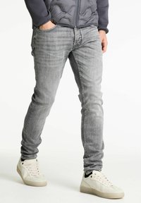 Jeans ajustados de color gris hechos de denim, con un sutil patrón de lavado. Combinados con zapatillas blancas y una chaqueta acolchada, solo vista frontal.