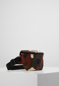 Marsupio mimetico in tessuto rosso, verde e beige, dotato di chiusura zip, tracolla nera regolabile e un piccolo logo.