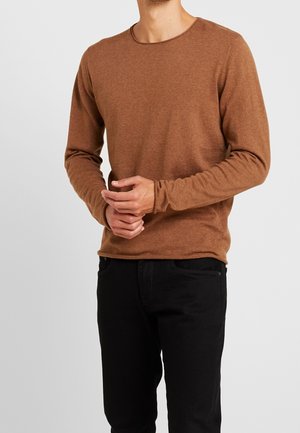 Braunes Langarm-T-Shirt mit Rundhalsausschnitt und schmalen Bündchen, getragen mit schwarzen Hosen. Der Stoff wirkt weich und strukturiert.