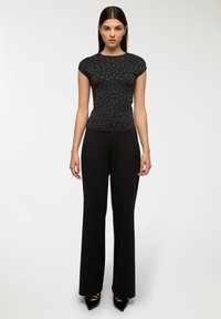 Czarna koszulka z krótkim rękawem z ozdobami w postaci srebrnych ćwieków, połączona z czarnymi spodniami o szerokich nogawkach. Gładki materiał i dopasowany krój.