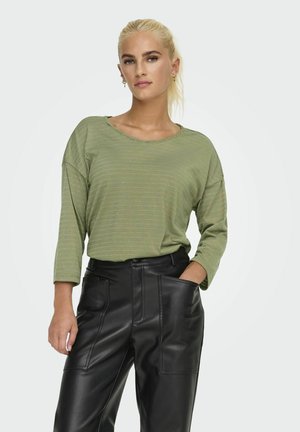 Top de manga larga a rayas verdes con un corte holgado y cuello redondo, combinado con pantalones de cuero negro de cintura alta que cuentan con detalles de bolsillos.