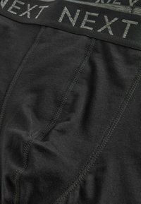 Black boxer briefs with stitched seams and a black waistband featuring the word "NEXT" in gray lettering.