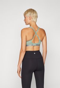 Sujetador deportivo en verde con un diseño texturizado, con tirantes entrecruzados y un cierre de gancho y ojal. Combinado con leggings negros de cintura alta.