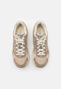 Beige sko til trening laget av mesh og semsket skinn, med hvite lisser, polstret krage og en tykk gummisåle. Aksenter i grå.