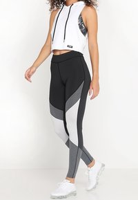 Leggings neri e grigi con pannelli geometrici, vita alta, abbinati a una felpa bianca corta con cappuccio e lacci.