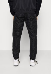 Joggers negros ajustados con cintura y puños elásticos, textura suave, bolsillos laterales y un detalle de marca mínimo. Llevados con zapatillas blancas.