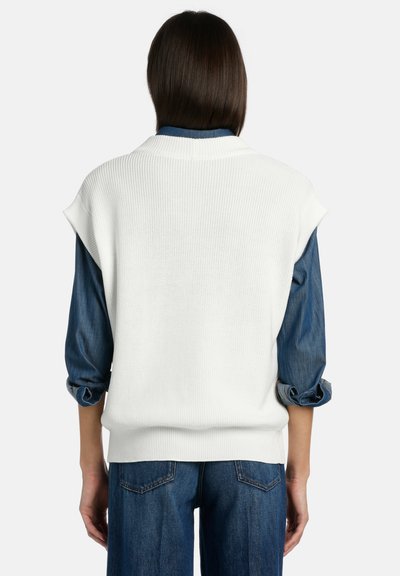Bela rebrasta brezrokavnica plastena preko modre denim srajce, z zavihanimi rokavi in sproščenim krojem, z okroglo izrezom.