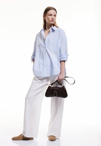 Camisa de botones a rayas azul claro, de corte holgado; pantalones anchos blancos; bolso marrón oscuro con detalles metálicos; zapatos beige tipo slip-on.